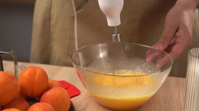 The process of making a pie at home. Close-up of a woman's hands beating eggs in a glass bowl. The process of mixing ingredients for the dough with an electric mixer with a whisk attachment.