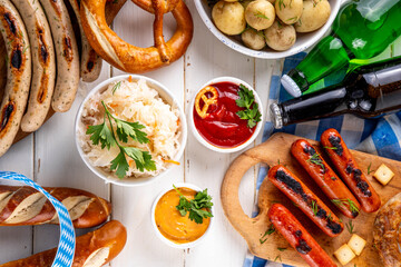 Fototapeta premium Oktoberfest picnic and barbecue food, bavarian party menu, bavarian sausages, pretzels, potato, sauerkraut, beer bottles, with picnic basket, checkered napkin tablecloth, Oktoberfest festive ribbon