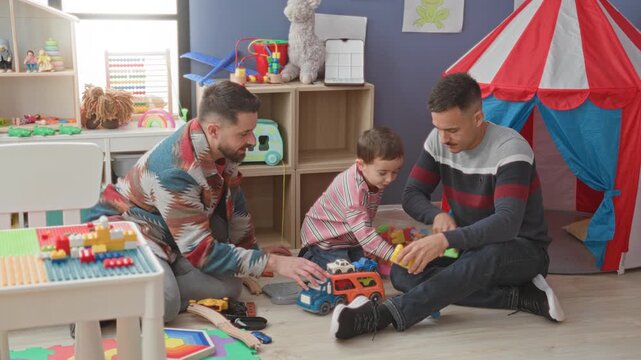 Boy and two men sit on floor, hands stacking colorful toy blocks and pushing a toy truck in a playroom inside a building; family bonding joy.