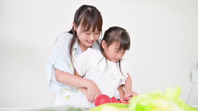 [スローモーション]キッチンで料理を通して包丁の使い方を学ぶ母親（親子）食育を実践する母親と小学生や幼児の女の子動画