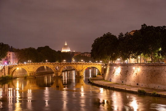 Beautiful illuminated view of Rome, Italy with Saint Peters Basiica, historic architecture, bridges and Tiber River under evening sky. 