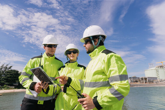 Engineers in safety gear collaborating on project plans near the water on a sunny day