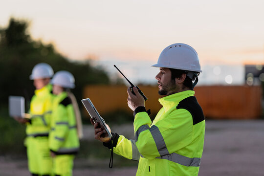 Construction workers in high visibility gear communicating on a job site at dusk with tools and equipment