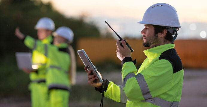 Construction workers collaborating on site with communication devices in high visibility gear at dusk