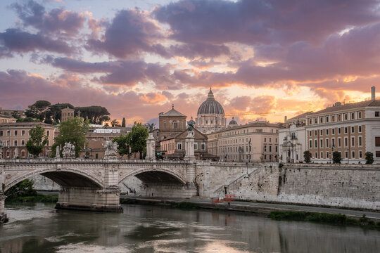 Beautiful illuminated view of Rome, Italy with Saint Peters Basiica, historic architecture, bridges and Tiber River under evening sky. 