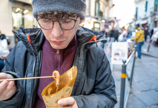 Naples, italy. December 27, 2024. Man enjoying a cuoppo of fried shrimp from a street food vendor, experiencing local culture in spaccanapoli, naples