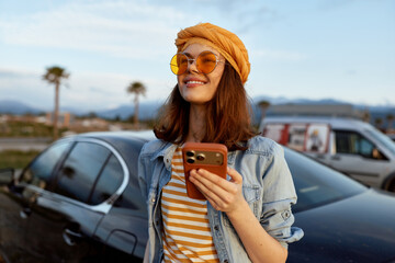 Naklejka premium A woman lifestyle casual travel sunny phone sunglasses turban denim outdoor scene with a cheerful pose near parked cars in bright daylight.