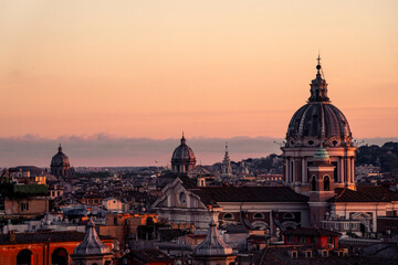 Obraz premium Historic city skyline with domed church and terracotta rooftops at sunset during golden hour, warm evening light
