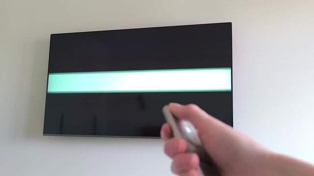Hand holding a remote control turns off a television showing a green chroma key screen. The TV is angled on the wall as the screen switches off. Concept of smart TV mockup, remote control