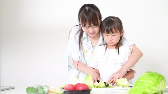 キッチンで料理を通して包丁の使い方を学ぶ母親（親子）食育を実践する母親と小学生や幼児の女の子動画