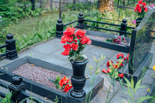 Well-maintained family memorial complex with polished granite slabs, a neat black fence and flowers in a cemetery