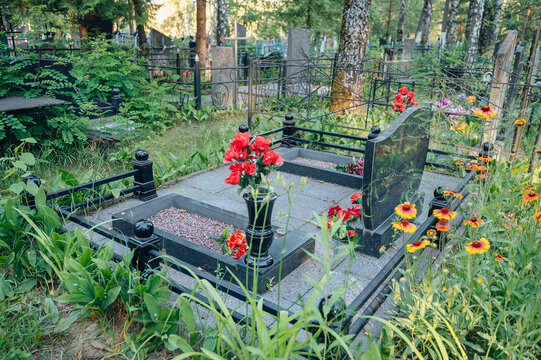 Well-maintained family memorial complex with polished granite slabs, a neat black fence and flowers in a cemetery