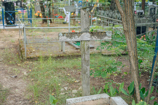 Wooden cross standing upright, in cemetery, with wooden cross, metal fence, flowers, trees, with wood, metal texture, from a ground-level perspective perspective.