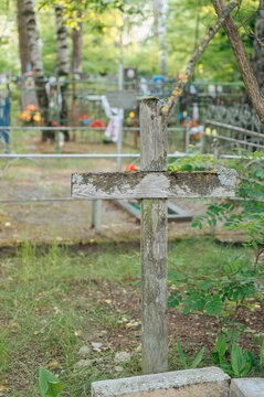 serene wooden cross standing upright in a cemetery with a metal fence and flowers, ground-level perspective, green and brown tones, religious imagery, memorial photography, cemetery scenes.