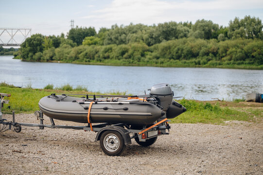 inflatable boat on trailer by calm riverbank side view with motor and grass near water in recreational boating setting for outdoor activities and serene outdoor.