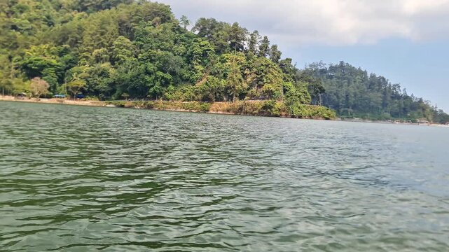 Scenic boat tour on a beautiful tropical lake viewing rural settlements and lush green mountains in the distance