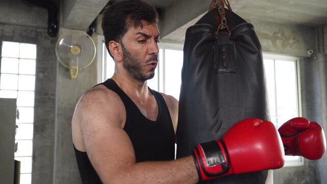 Muscular man training with a punching bag in a gym, wearing boxing gloves and focused on strength, fitness, boxing, kickboxing and intense workout performance.