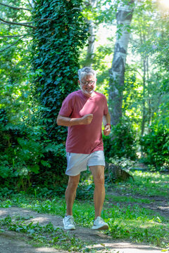Senior man jogging through a forest park trail to improve cardiovascular fitness, endurance, mobility, and overall health while maintaining an active outdoor lifestyle.