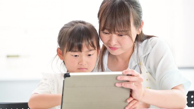タブレットを使って一緒に学習する母親と小学生の女の子・家庭で学ぶ親子のデジタルict教育のライフスタイル　画面を笑顔で見るクローズアップの縦動画