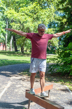 Senior man walking on a balance beam in an outdoor fitness park to develop stability, coordination, body awareness, lower body strength, and functional balance.