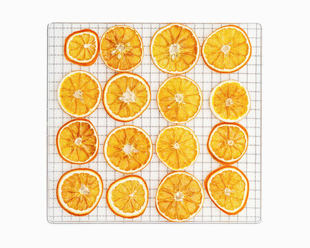 Natural dried oranges on grid for dryer on white background. Sliced and dried candied citrus fruit food. Minimal style top view aesthetic still life of aromatic vivid yellow round orange pieces.