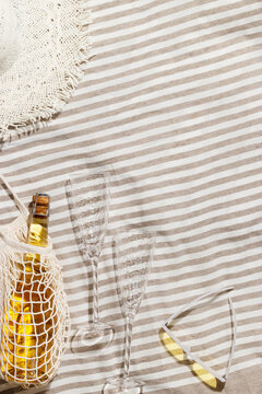 Summer rest flat lay of bottle of white champagne, yellow sunglasses, two wine glasses on cloth, outdoor scene at sunlight. Dining and celebration at beach, park picnic concept, top view, copy space.