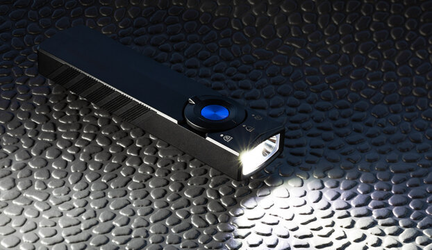 Rechargeable LED flashlight turn on while resting on a black textured mat