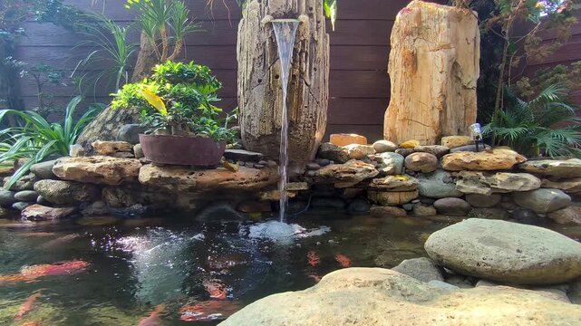 Serene koi pond garden with decorative stone waterfall fountain and lush green tropical plants in backyard scene