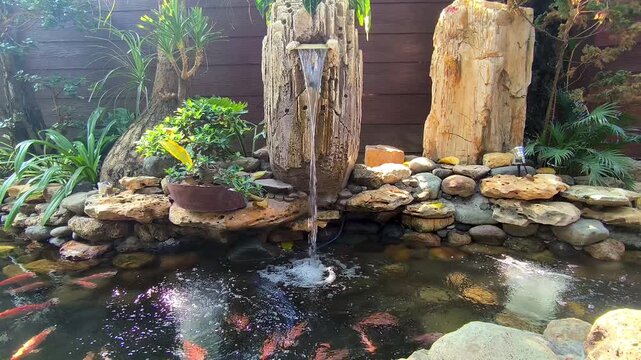 Serene koi pond garden with decorative stone waterfall fountain and lush green tropical plants in backyard scene
