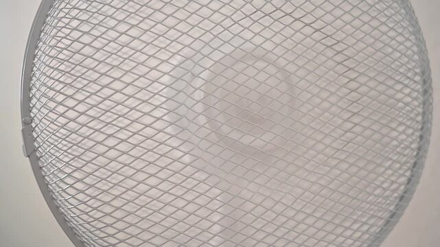 Close-up of a white electric fan grille with subtle motion blur effect