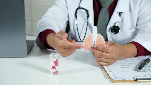A doctor explains the effectiveness of medication for lung diseases, asthma, and bronchitis to a patient. He holds a medicine bottle and an anatomical model of the lungs on the clinic table. The conce