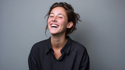 Fototapeta premium happy young woman with curly hair smiling brightly in a casual studio portrait against grey background