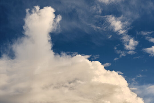 Tall fluffy cloud stretches up into deep blue sky with light wispy cirrus in background.
