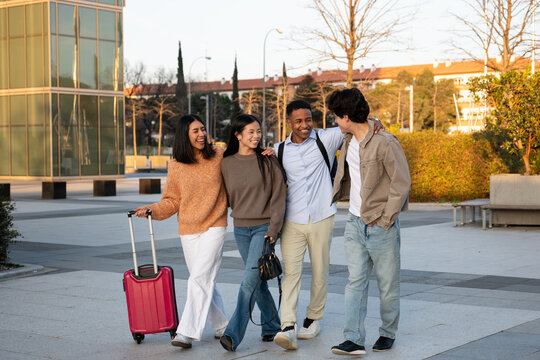 Diverse group of friends walking together with luggage, smiling and happy