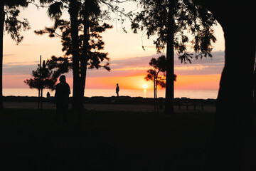 Naklejka premium Woman silhouette at sunset outdoors, relaxed lifestyle moment by water, warm hues, tranquil park setting