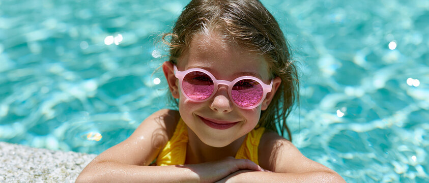 Portrait d'une jolie petite fille souriante portant des lunettes de soleil roses se baignant dans une piscine pendant les vacances d'&eacute;t&eacute;
