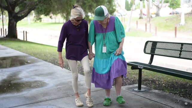 A mature daughter and her elderly mother enjoy a walk in the park while talking and laughing, sharing stories and memories together.