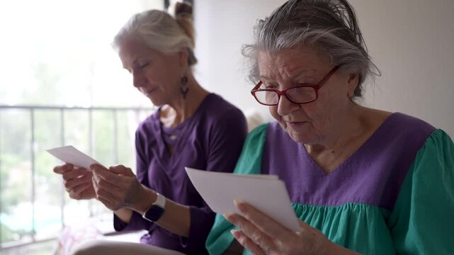 Mature daughter spends time with elderly mother at a senior care facility. They share photos and talk about memories from the past.