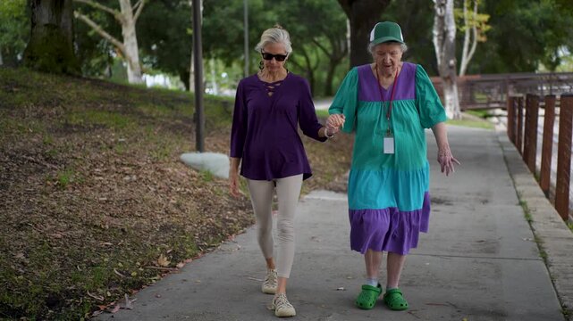 Elderly mother and mature daughter enjoy a visit in a park, sharing stories and laughter while walking together on a sunny day.