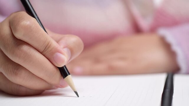 Close up slow motion of female hand writing with pencil on paper, illustrating study, work, or creative process.