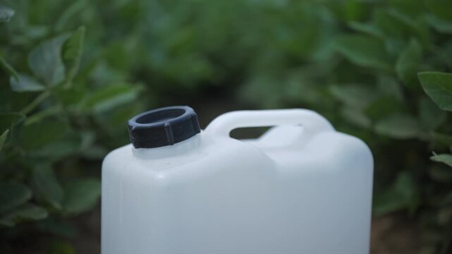 Plastic agrochemical canister standing in a healthy soybean field ready for crop treatment. Farming, plant protection and precision agriculture theme. 4K.