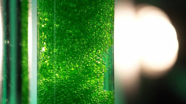 Green liquid with bubbles inside transparent container glowing softly close up with bright light background glowing dark