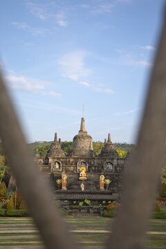 Magnificent mini replica of Borobudur temple surrounded by lush gardens, pathways, and golden Buddha statues under a blue sky at Brahma Vihara Arama monastery in Bali.