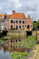 Obraz premium Historic canal house with water lilies in Franeker Friesland, Netherlands, traditional Dutch architecture and bridge
