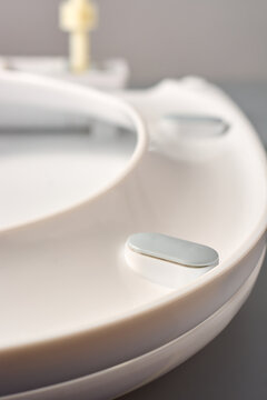 white plastic toilet seat with grey rubber bumper pad close-up on grey background, side view with soft focus, bathroom hardware replacement