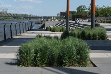 Modern pedestrian embankment in Warsaw features contemporary urban design. Green decorative grass grows in paved promenade near river. Scenic European architecture for travel and landscaping. © dimetradim