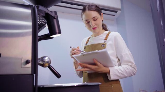 Female roaster taking notes on clipboard at roasting machine
