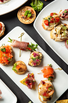 An overhead shot of a catering platter with various gourmet finger food appetizers, including salmon and prosciutto crostini on white plates