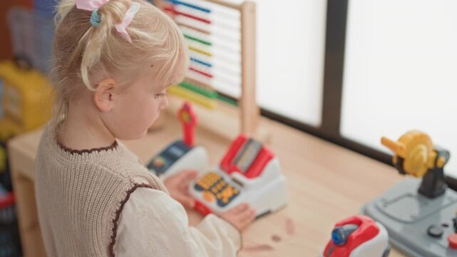 Girl pressing a toy cash register button with her hand at a wooden play counter near a window in a building; curiosity.