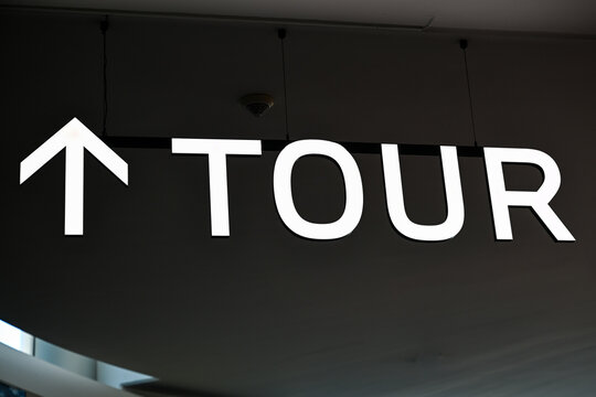Illuminated "TOUR" directional sign with arrow on dark ceiling
